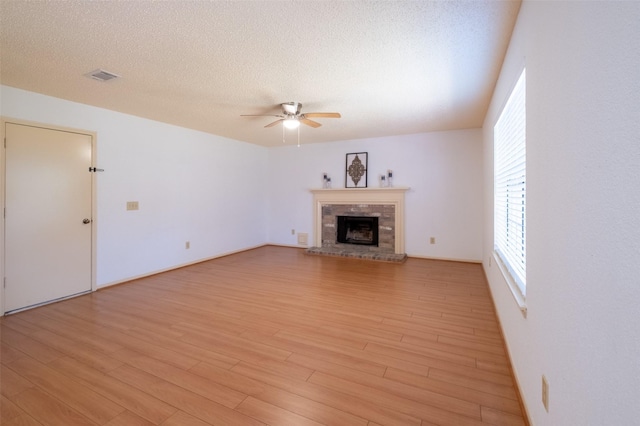 unfurnished living room with a fireplace, a ceiling fan, light wood finished floors, and a textured ceiling