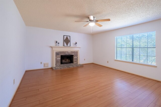 unfurnished living room featuring baseboards, light wood-style flooring, a fireplace, a textured ceiling, and a ceiling fan