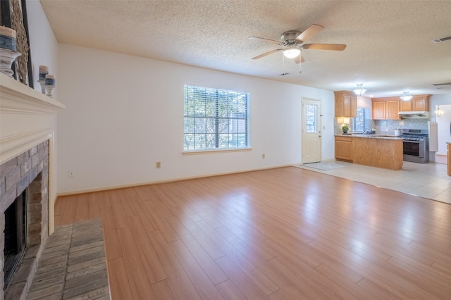 unfurnished living room with light wood finished floors, a fireplace, a textured ceiling, and ceiling fan