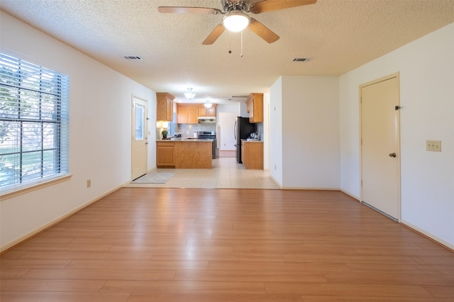 unfurnished living room with a textured ceiling, visible vents, light wood finished floors, and ceiling fan