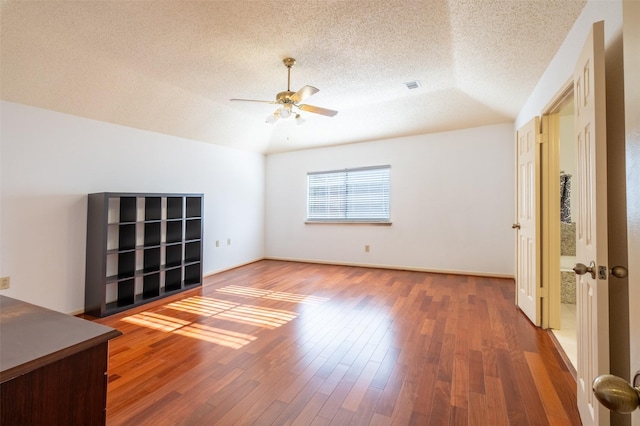 empty room with visible vents, ceiling fan, vaulted ceiling, wood finished floors, and a textured ceiling