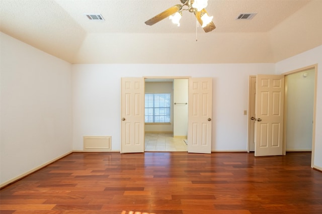 unfurnished room with a raised ceiling, wood finished floors, visible vents, and vaulted ceiling