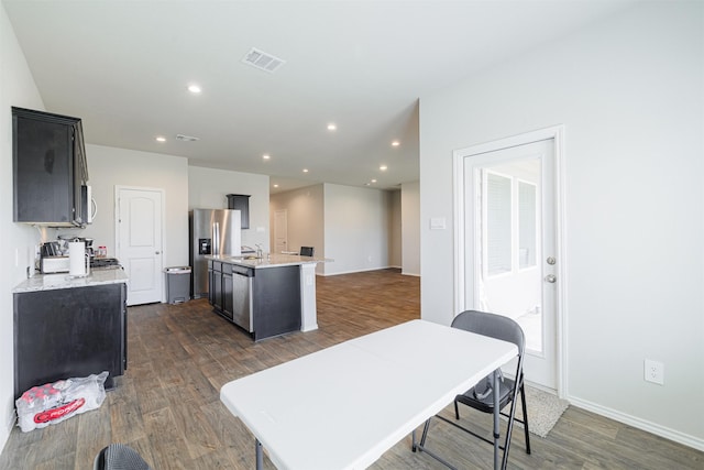 kitchen featuring visible vents, stainless steel fridge, a center island with sink, and dark wood-style flooring