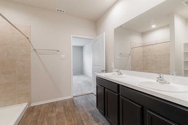 full bath featuring a tile shower, visible vents, wood finished floors, and a sink