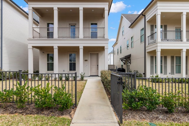 view of front of house with a balcony, covered porch, a fenced front yard, and stucco siding