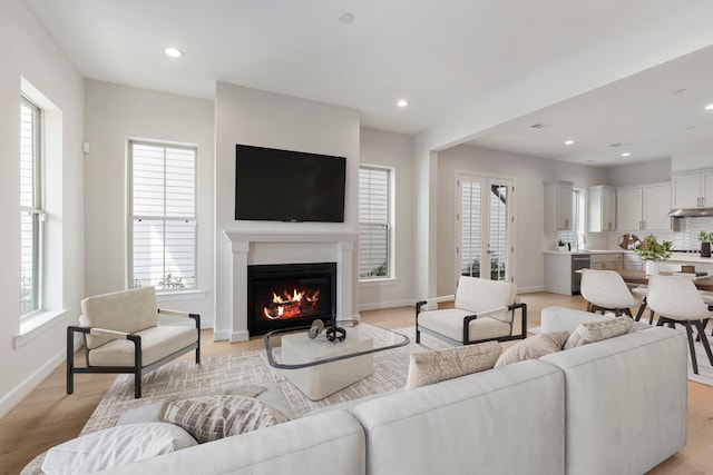 living room with a glass covered fireplace, recessed lighting, light wood-type flooring, and baseboards