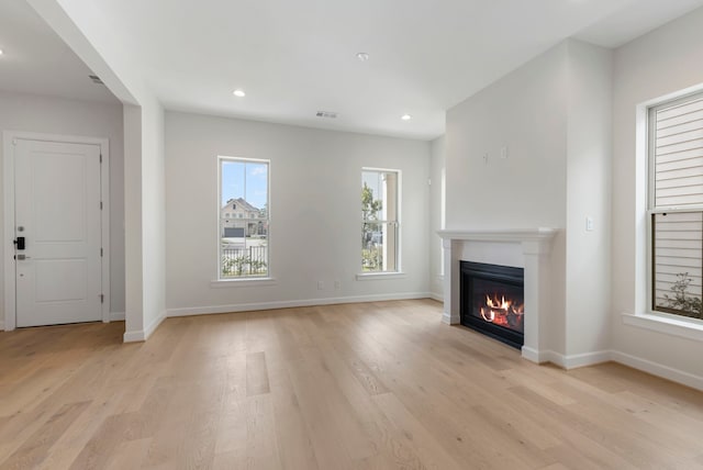 unfurnished living room featuring visible vents, baseboards, a glass covered fireplace, and light wood finished floors