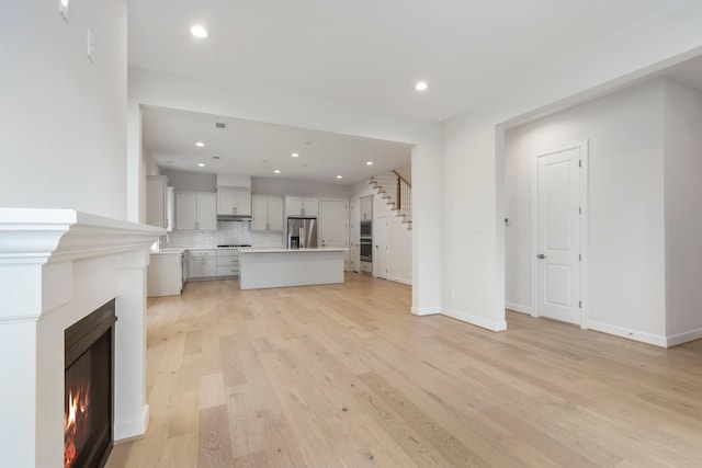 unfurnished living room with stairs, recessed lighting, light wood-type flooring, and a lit fireplace