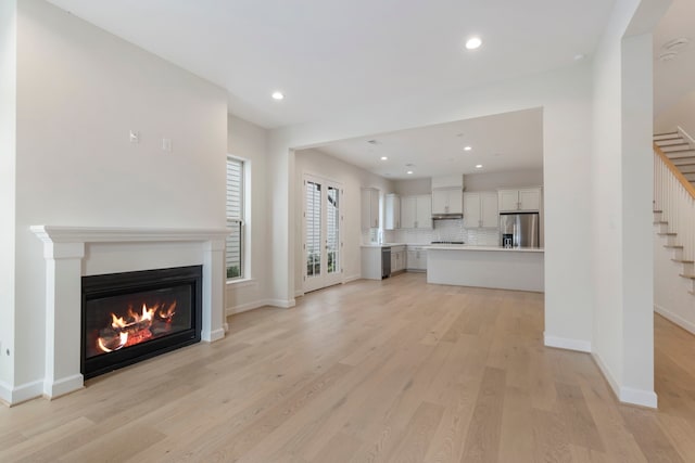 unfurnished living room featuring baseboards, a glass covered fireplace, stairs, and light wood finished floors