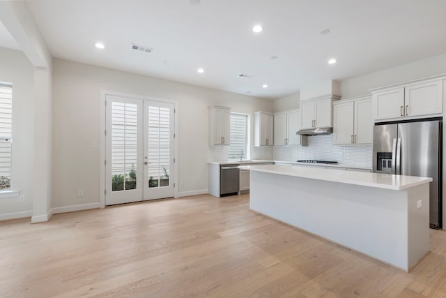 kitchen featuring a kitchen island, under cabinet range hood, light countertops, decorative backsplash, and stainless steel appliances