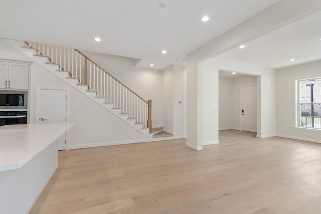 unfurnished living room with stairs, recessed lighting, light wood-type flooring, and baseboards