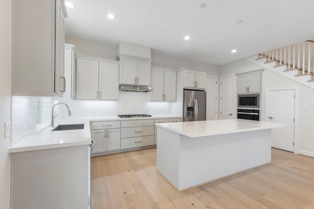 kitchen with a sink, light wood-type flooring, black appliances, and under cabinet range hood