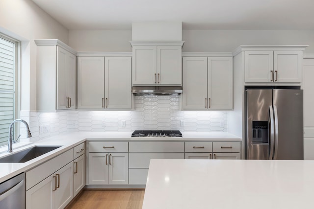 kitchen featuring a sink, under cabinet range hood, light wood-style floors, appliances with stainless steel finishes, and light countertops