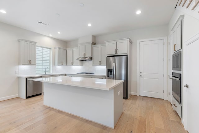 kitchen with visible vents, a kitchen island, stainless steel appliances, light countertops, and under cabinet range hood