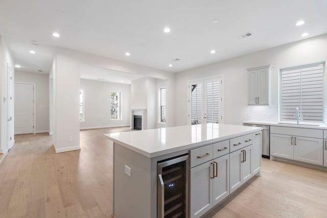 kitchen featuring light wood finished floors, visible vents, wine cooler, gray cabinets, and a sink