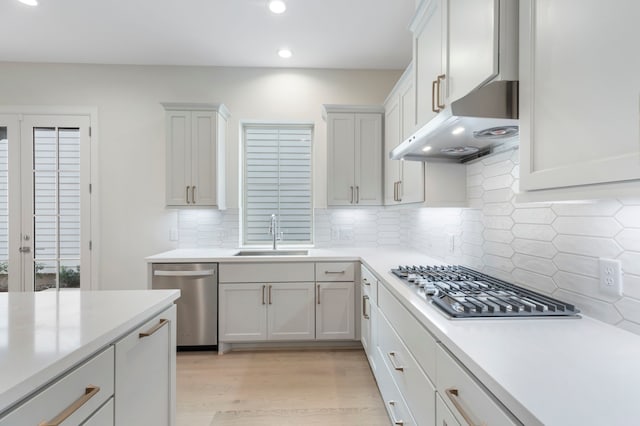 kitchen with under cabinet range hood, light wood-type flooring, light countertops, stainless steel appliances, and a sink