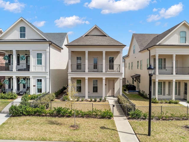 neoclassical / greek revival house featuring a fenced front yard, a front lawn, a balcony, and roof with shingles