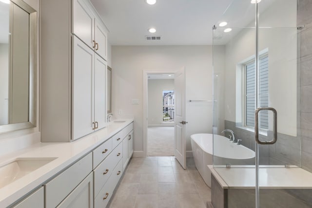 full bathroom with visible vents, double vanity, a freestanding tub, recessed lighting, and a sink