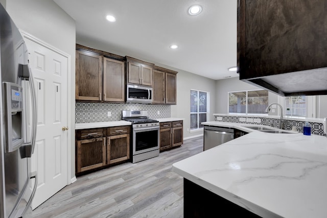 kitchen with light wood finished floors, a sink, decorative backsplash, dark brown cabinetry, and stainless steel appliances