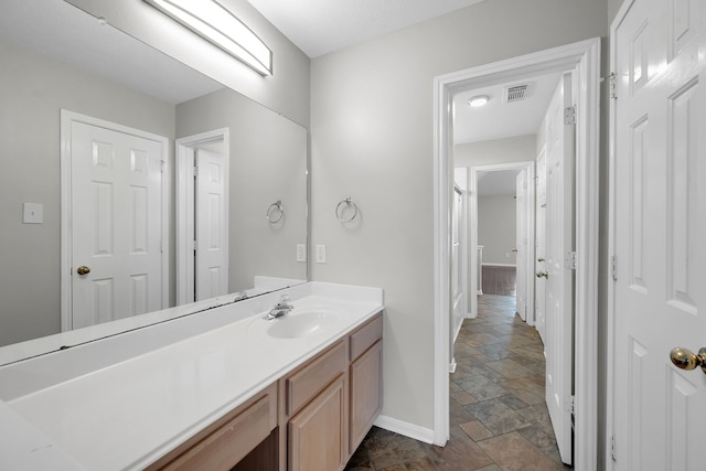 bathroom featuring visible vents, baseboards, vanity, and stone finish floor