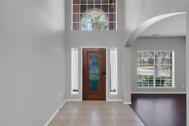 foyer with tile patterned flooring, arched walkways, visible vents, and baseboards