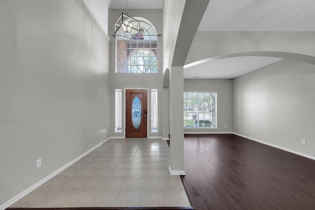 foyer featuring a notable chandelier, wood finished floors, arched walkways, a high ceiling, and baseboards