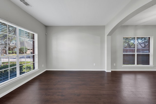 unfurnished room with arched walkways, visible vents, baseboards, and wood finished floors