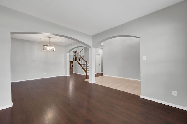 unfurnished room with baseboards, arched walkways, wood finished floors, and stairs