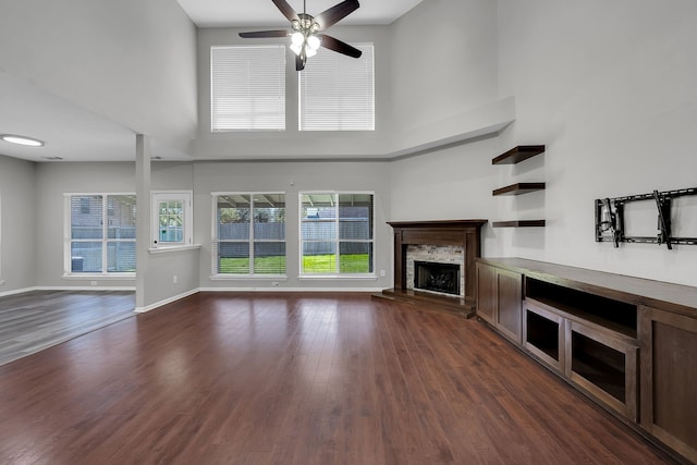 unfurnished living room featuring a towering ceiling, baseboards, dark wood finished floors, and a fireplace