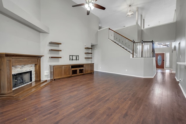 unfurnished living room featuring dark wood-type flooring, stairway, a high ceiling, a fireplace, and baseboards