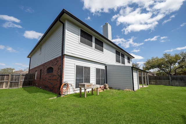 back of house with brick siding, a chimney, a fenced backyard, and a lawn