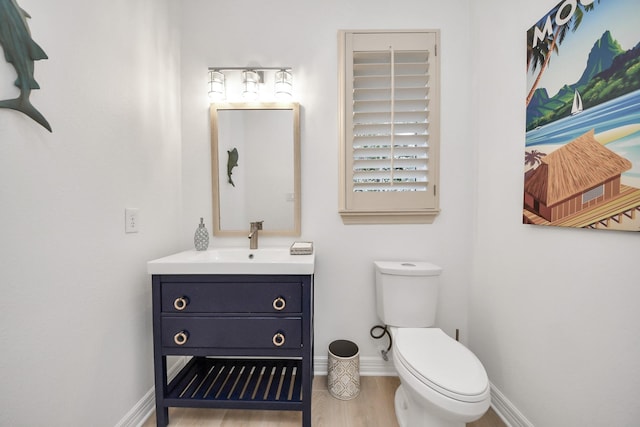 bathroom with toilet, vanity, baseboards, and wood finished floors