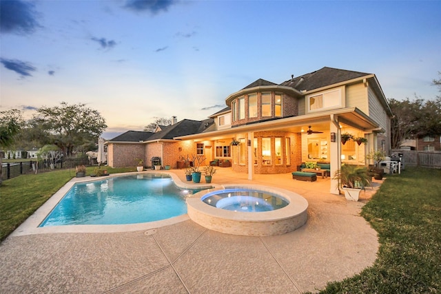 rear view of house with a lawn, a pool with connected hot tub, a patio, a fenced backyard, and brick siding