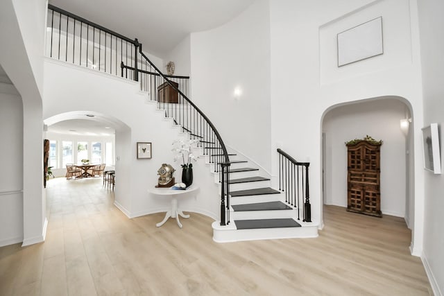 interior space with stairs, wood finished floors, arched walkways, and a towering ceiling