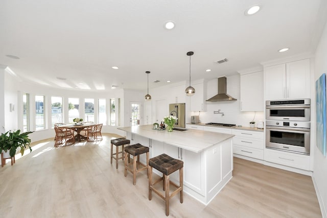 kitchen featuring visible vents, wall chimney range hood, stainless steel appliances, light countertops, and decorative backsplash