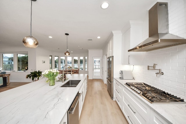 kitchen with a sink, appliances with stainless steel finishes, white cabinets, wall chimney range hood, and decorative backsplash