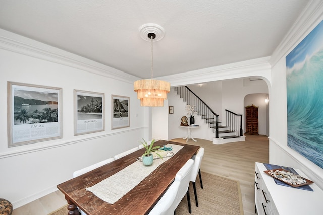 dining space with light wood finished floors, crown molding, stairs, an inviting chandelier, and arched walkways