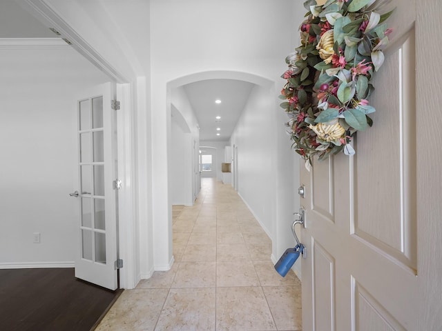 hallway featuring arched walkways, light tile patterned floors, recessed lighting, and baseboards