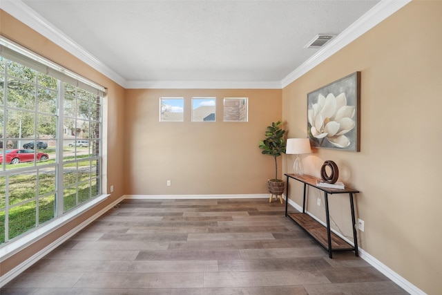 spare room featuring ornamental molding, wood finished floors, visible vents, and baseboards