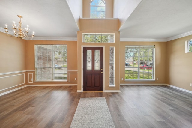 foyer entrance with a chandelier, a wainscoted wall, ornamental molding, and wood finished floors