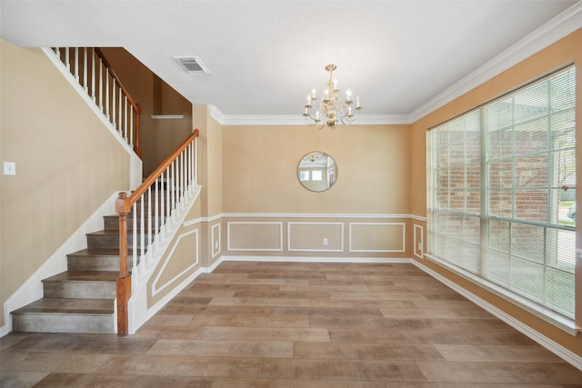 unfurnished dining area featuring visible vents, a notable chandelier, wood finished floors, and crown molding