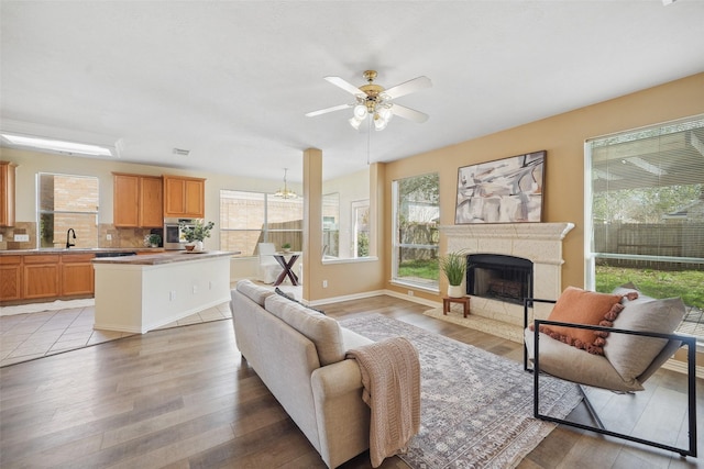 living room with a high end fireplace, a ceiling fan, light wood-type flooring, and a wealth of natural light