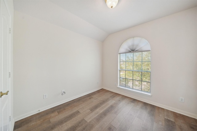 spare room with vaulted ceiling, baseboards, and wood finished floors