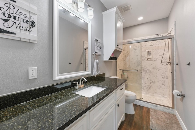 bathroom with visible vents, toilet, wood finished floors, a shower stall, and vanity