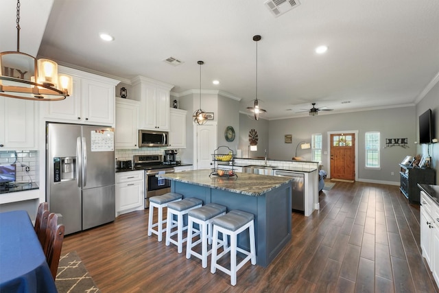 kitchen with visible vents, ceiling fan with notable chandelier, a center island, stainless steel appliances, and decorative backsplash