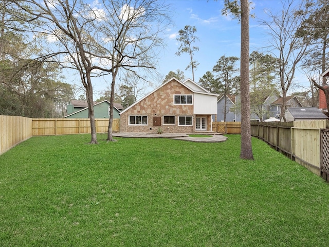 rear view of house featuring stone siding, a lawn, a patio, and a fenced backyard