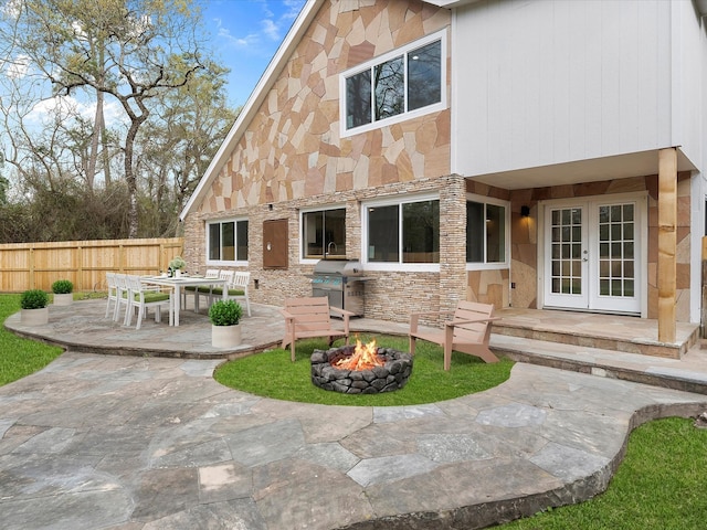 rear view of property with fence, french doors, stone siding, a fire pit, and a patio area