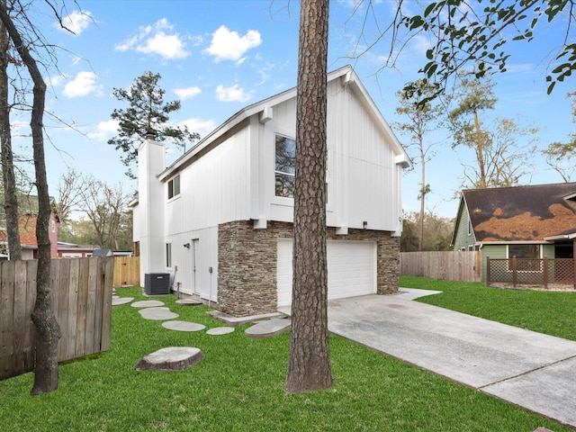 view of side of property featuring a lawn, driveway, stone siding, central AC, and fence