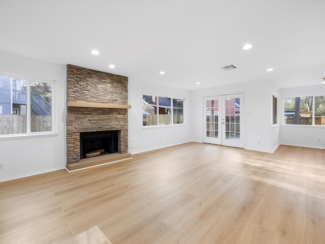 unfurnished living room featuring a stone fireplace, french doors, visible vents, and light wood finished floors