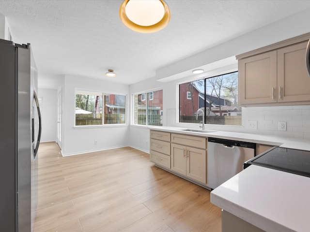 kitchen featuring a sink, decorative backsplash, stainless steel appliances, light wood-type flooring, and a wealth of natural light